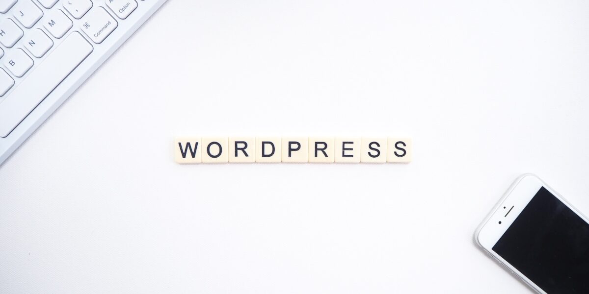 A white desk with a Mac keyboard and iPhone, with "Wordpress" spelled out using Scrabble tiles in the center.