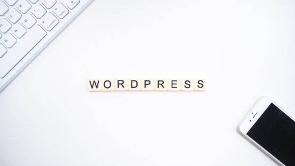 A white desk with a Mac keyboard and iPhone, with "Wordpress" spelled out using Scrabble tiles in the center.