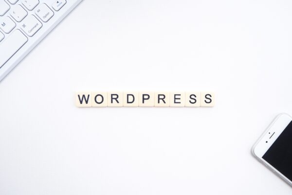 A white desk with a Mac keyboard and iPhone, with "Wordpress" spelled out using Scrabble tiles in the center.